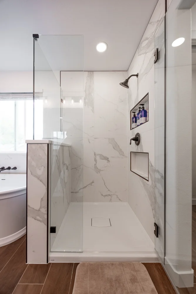 Marble-look walk-in shower with frameless glass and storage niches