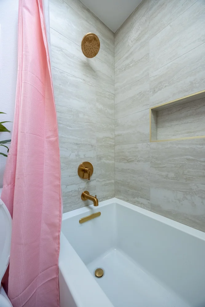 Pink-and-gold children’s bathroom with deep tub and tiled shower walls